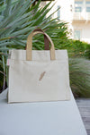 Beige tote bag with a sprig design on a white surface outdoors