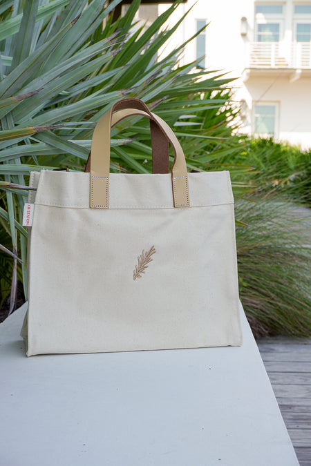 Beige tote bag with a sprig design on a white surface outdoors